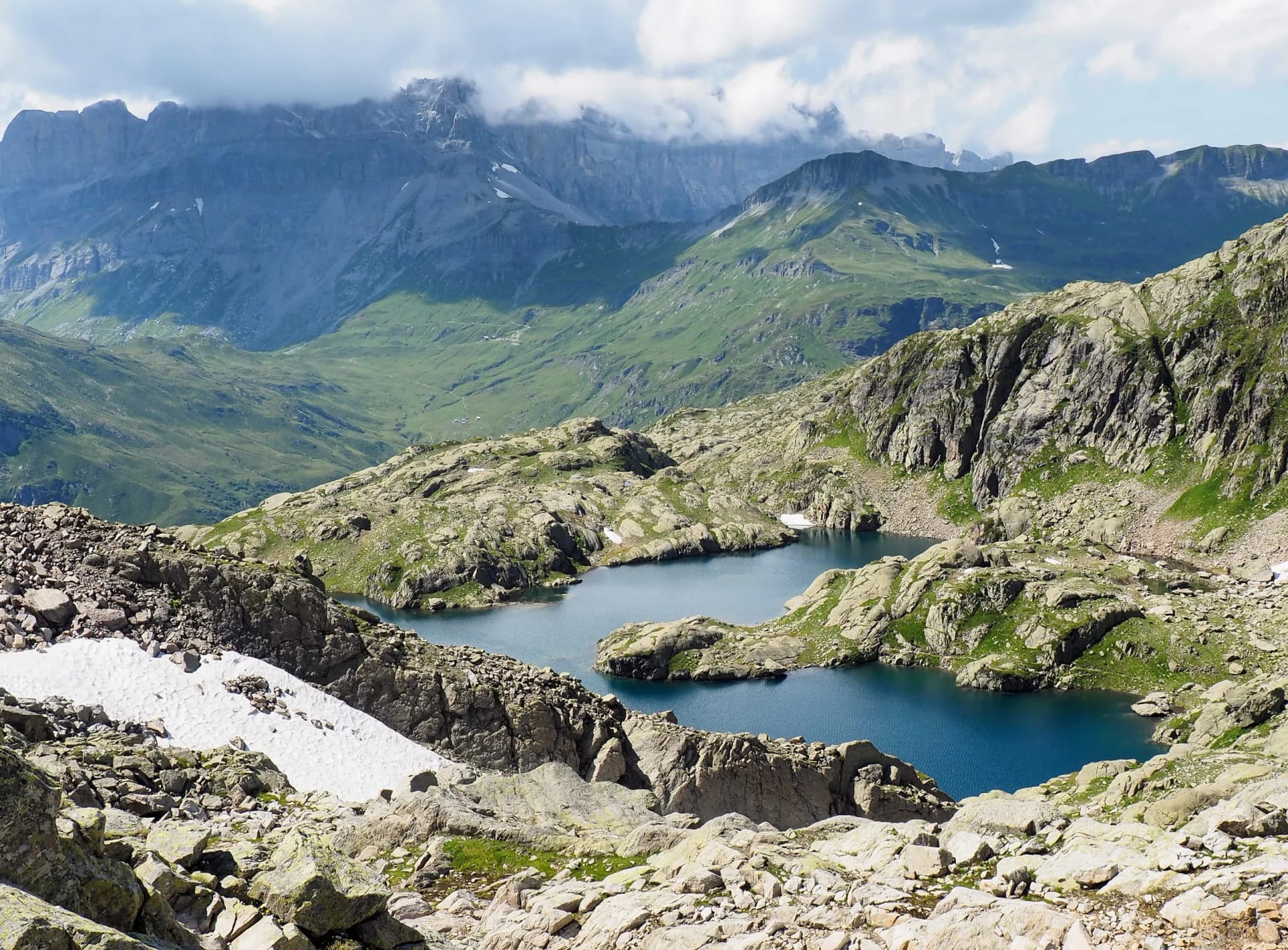 Alpine tarns above Chamonix with rocky foreground, green slopes, and distant mountains under clouds.