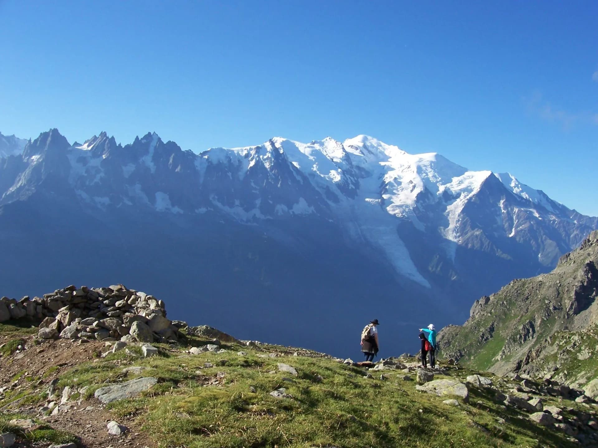 Hikers on grassy ridge overlooking snow-capped mountains, Le Brévent.