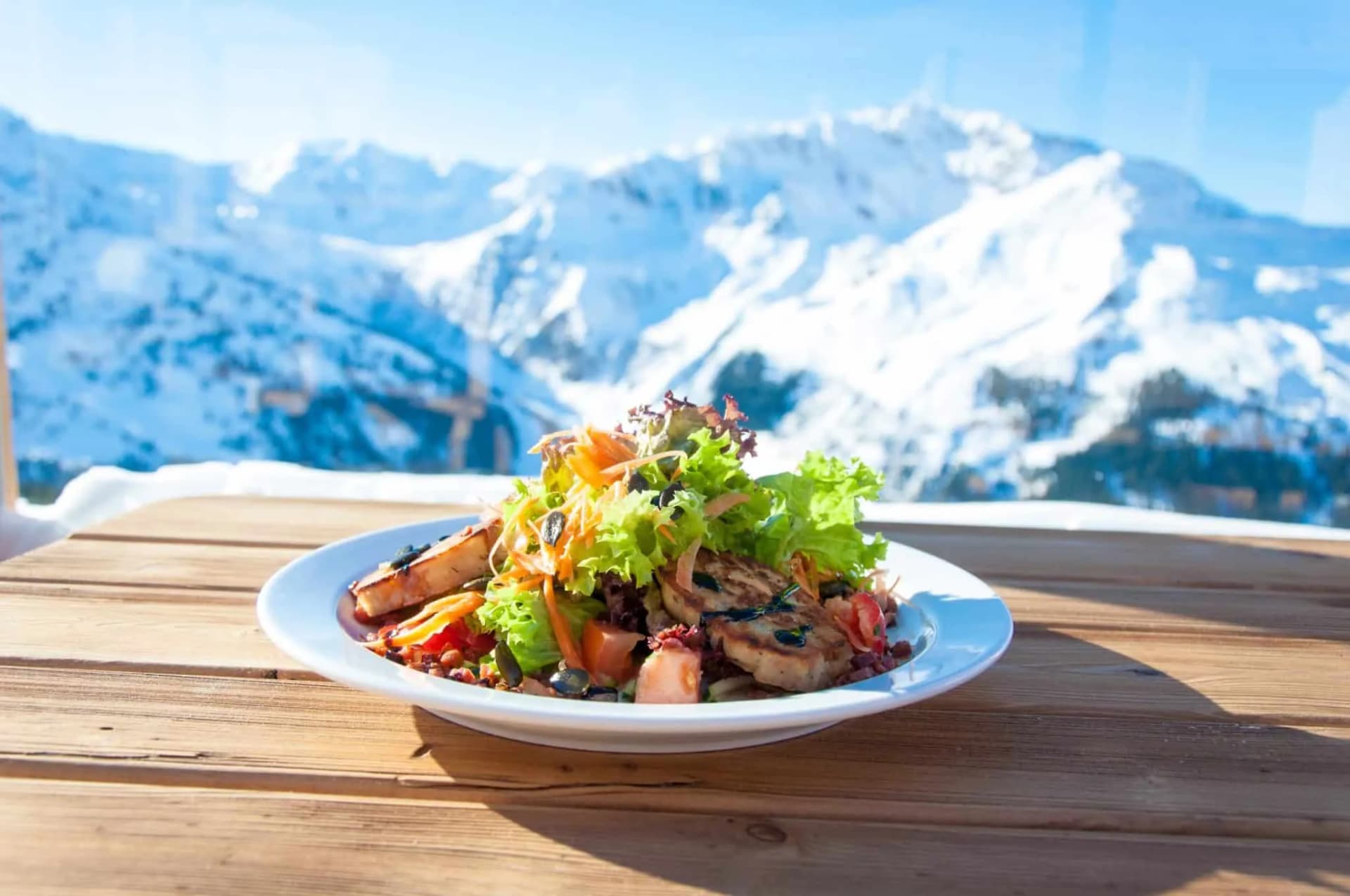 Salad with grilled protein on wooden table overlooking snow-covered mountains