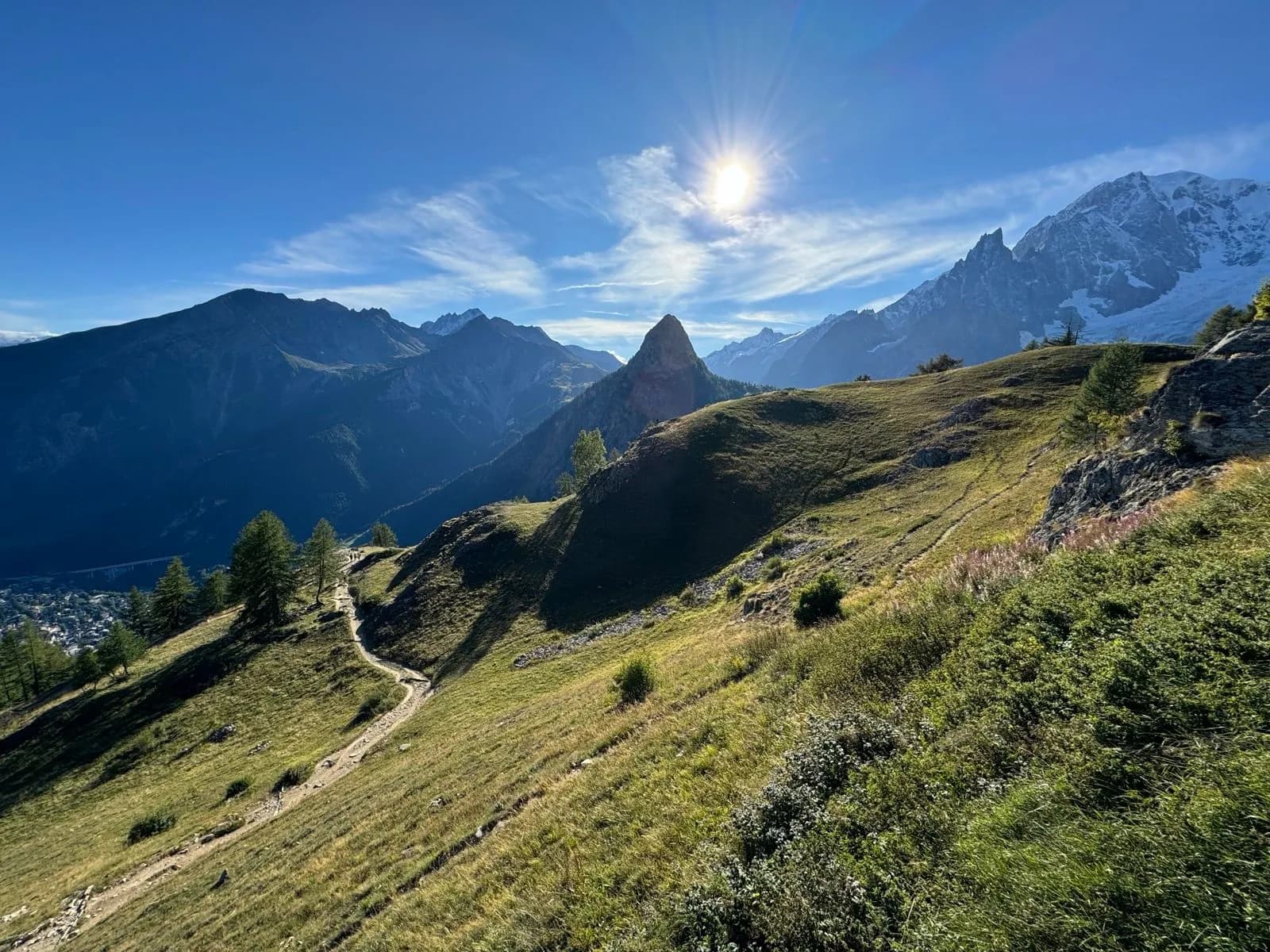 Hiking trail on grassy slope toward Rifugio Bonatti with sunny alpine peaks