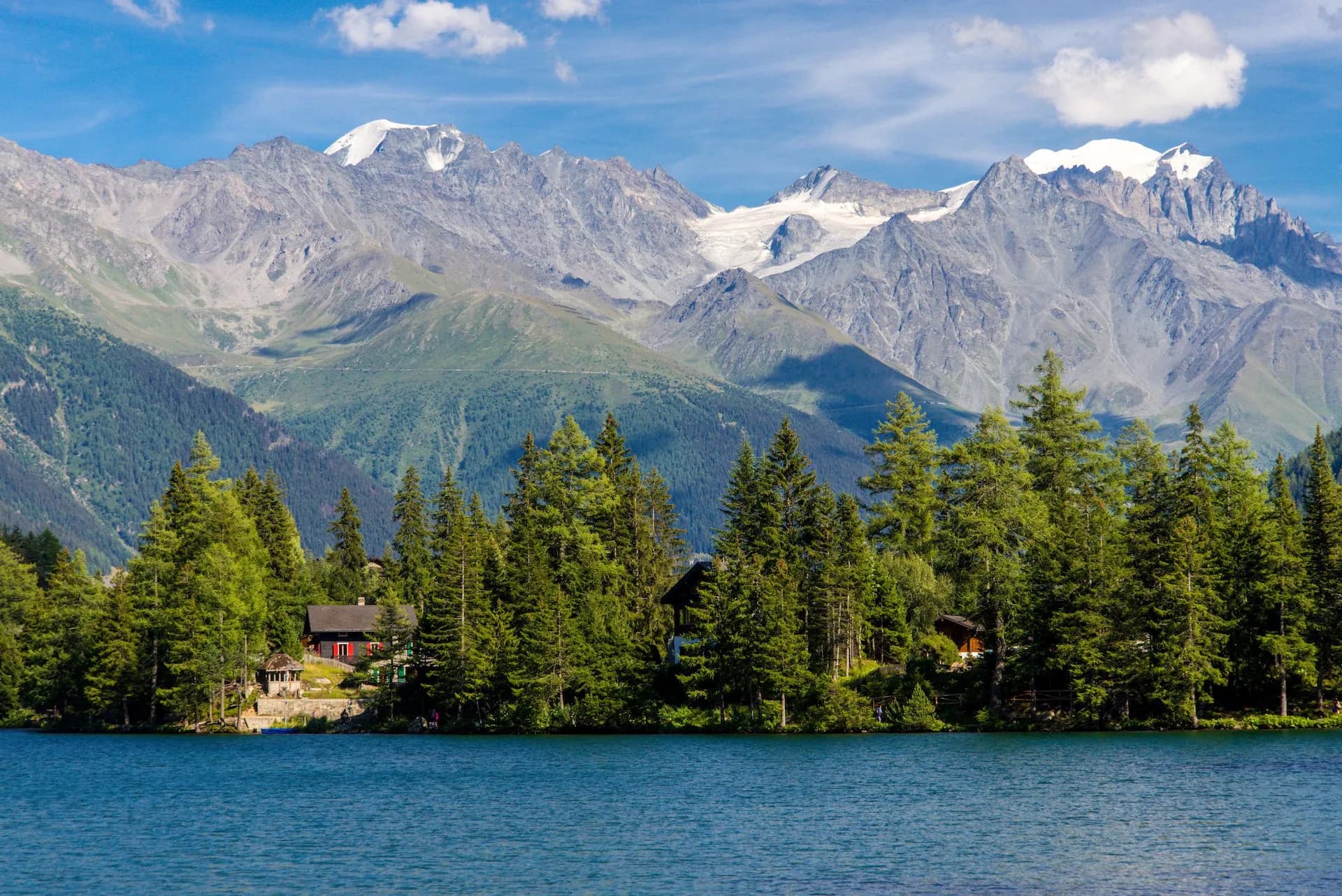 Alpine mountain lake Champex Lac with snow-capped peaks, pine forest, and lakeside cabin.