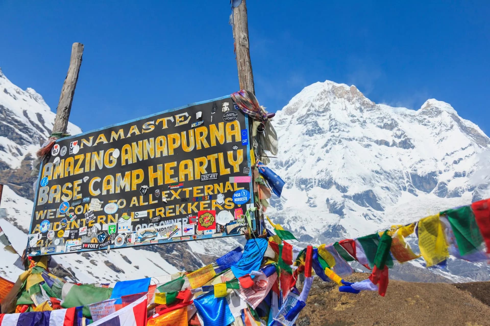 Annapurna Base Camp sign with prayer flags and Annapurna South snow-capped mountain, Nepal.