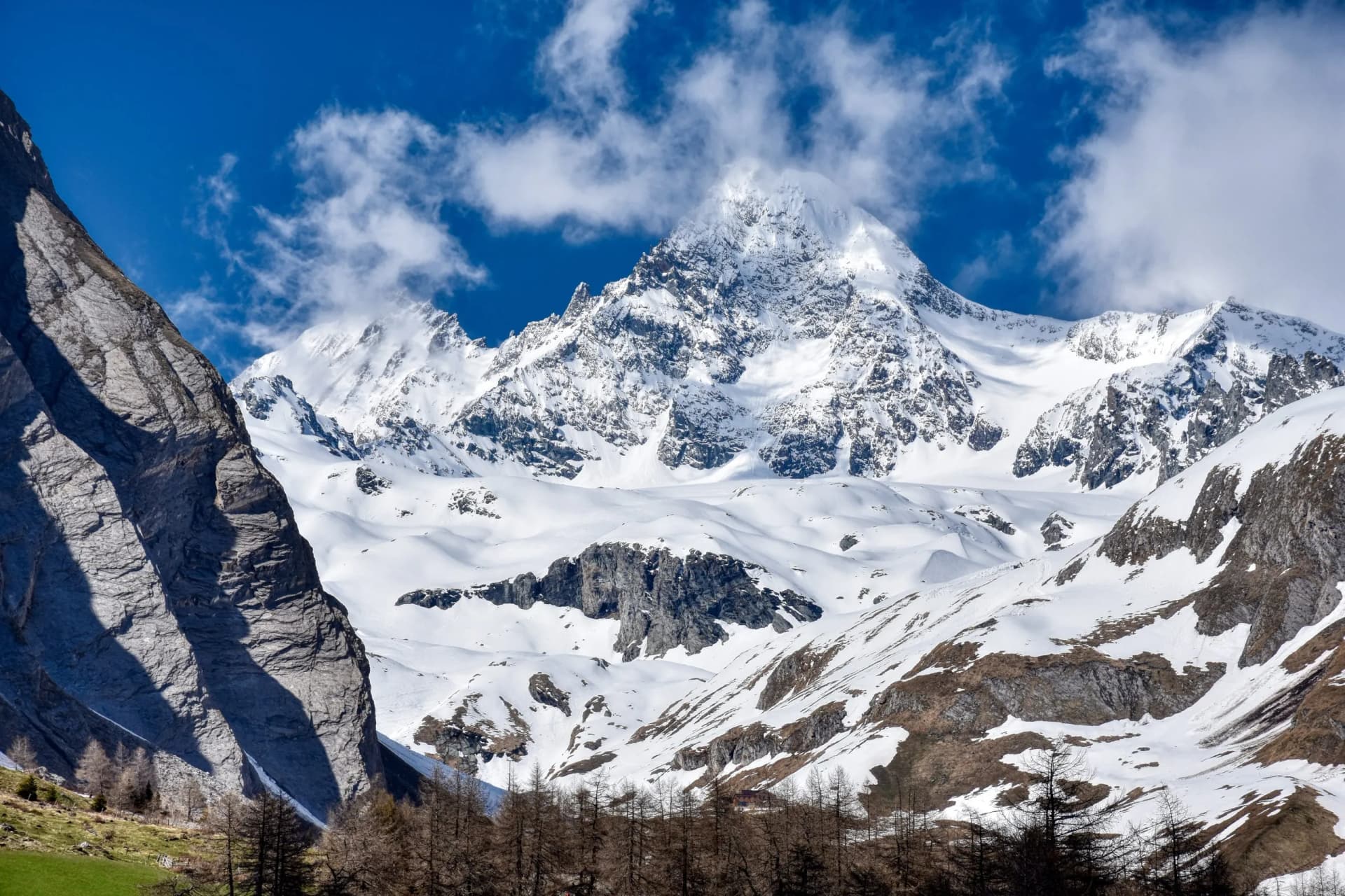 Snow-covered Grossglockner mountain peak under a bright blue sky with white clouds in winter.
