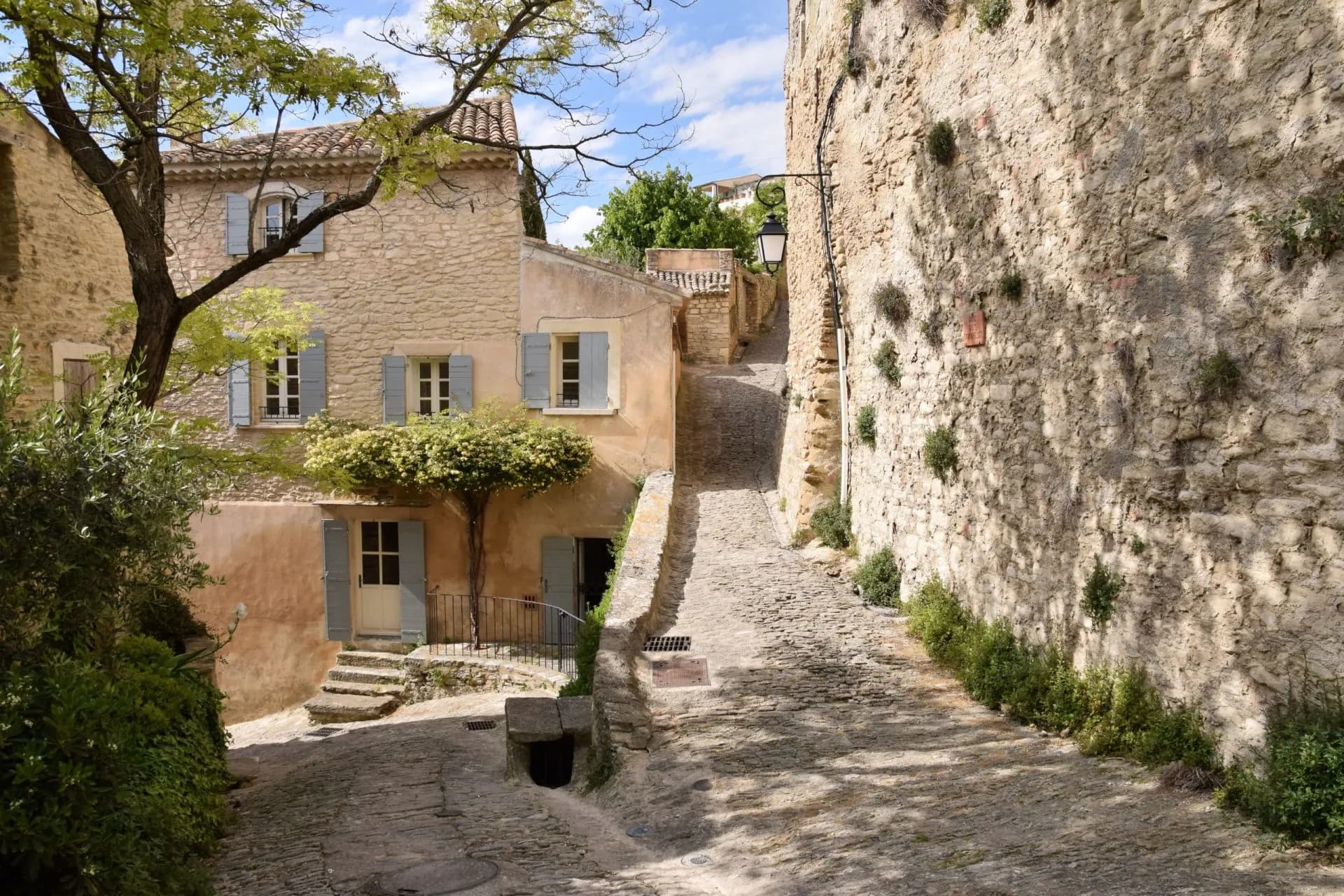 Cobblestone street climbing between stone buildings in Gordes town under a sunny sky.