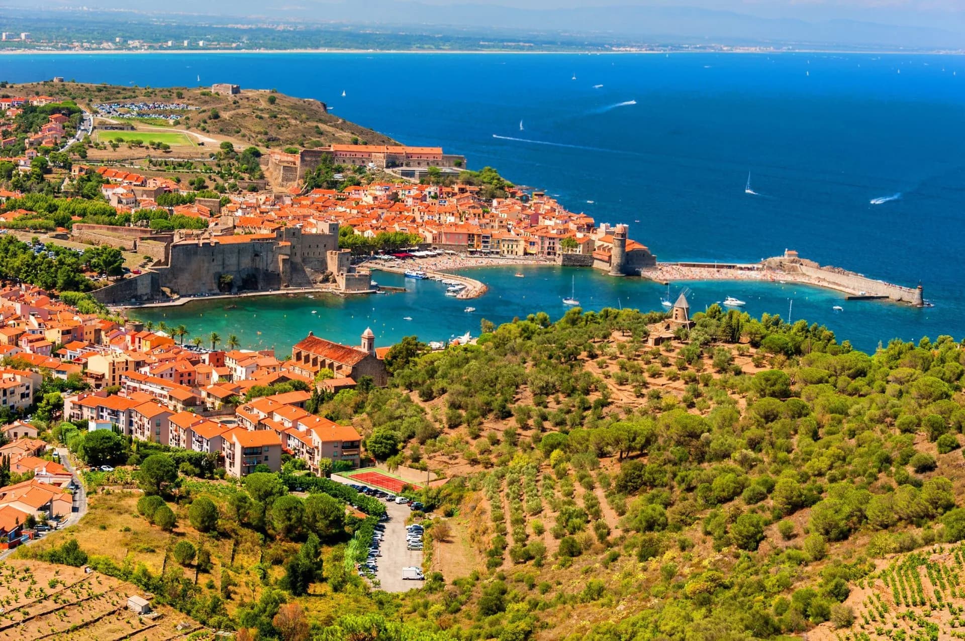 Coastal town of Collioure with terracotta roofs, harbor, and blue Mediterranean Sea.