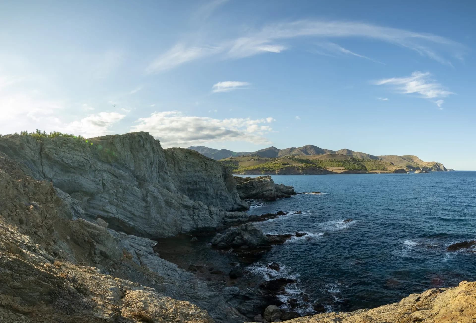 Rocky coastline near Llancà with steep cliffs meeting the deep blue sea under a bright sky.
