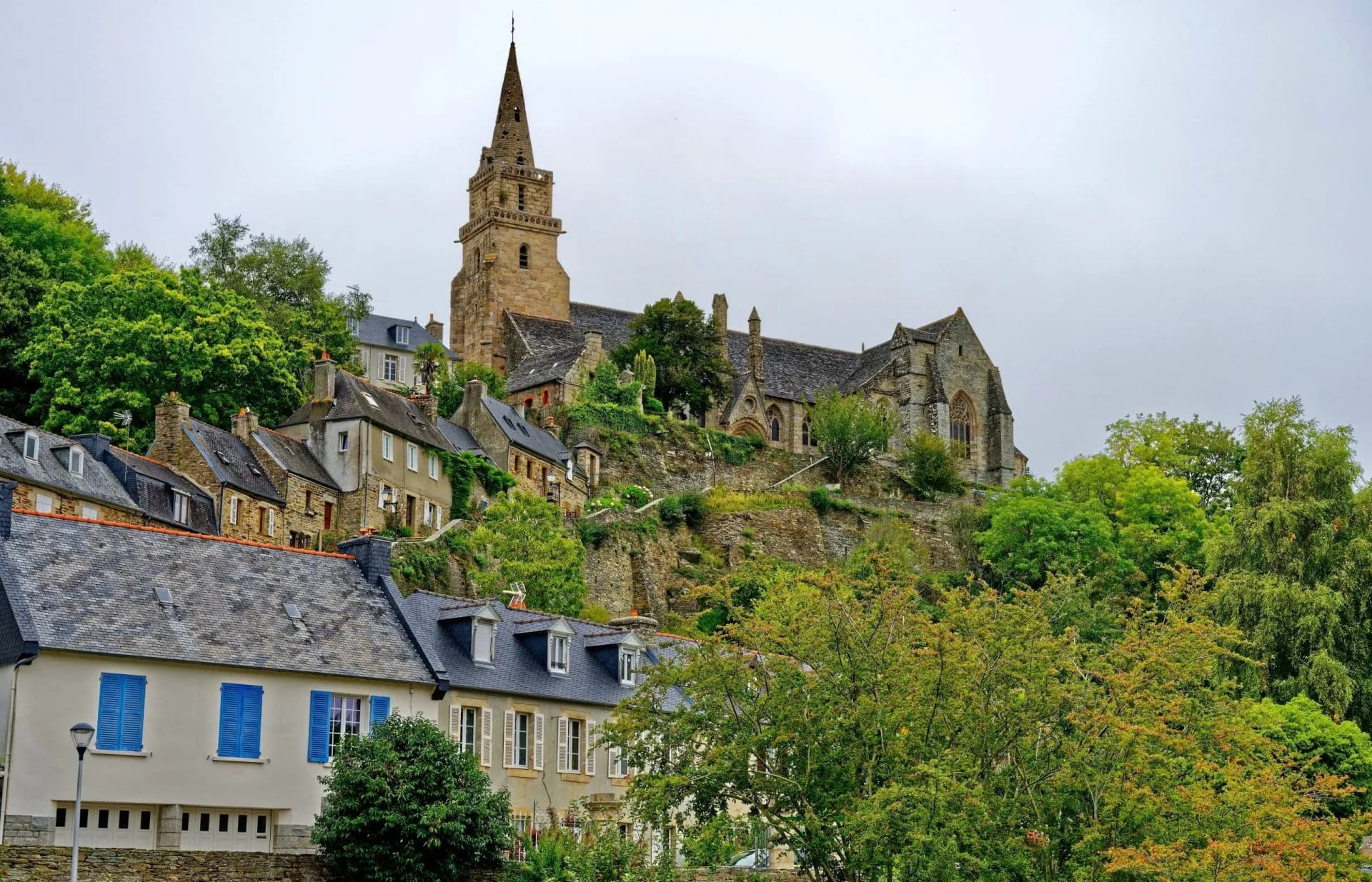 Stone church with spire overlooking hillside houses with slate roofs in Brelevenez.