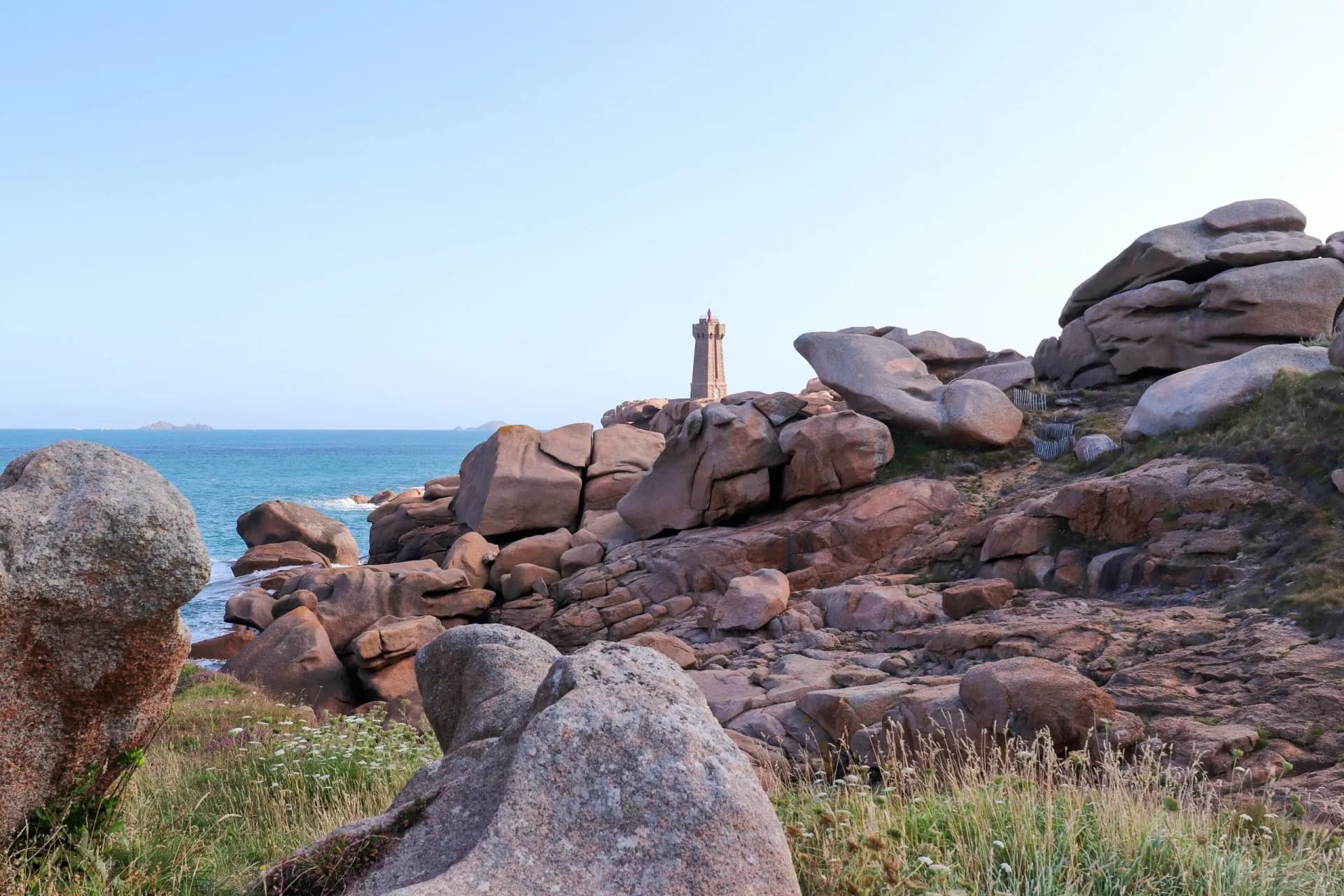 Lighthouse on rocky coast with pink boulders overlooking the blue sea near Ploumanac'h.