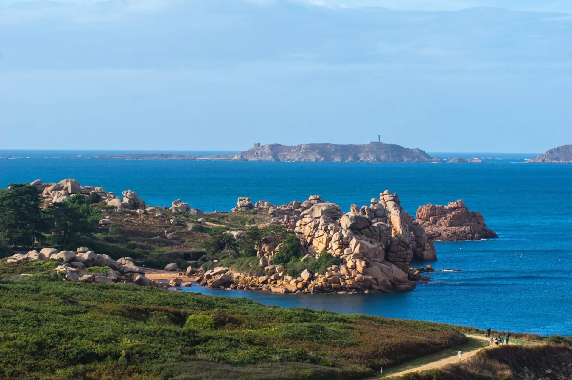 Coastline in Perros-Guirec with granite boulders, green scrubland, and islands with a lighthouse.