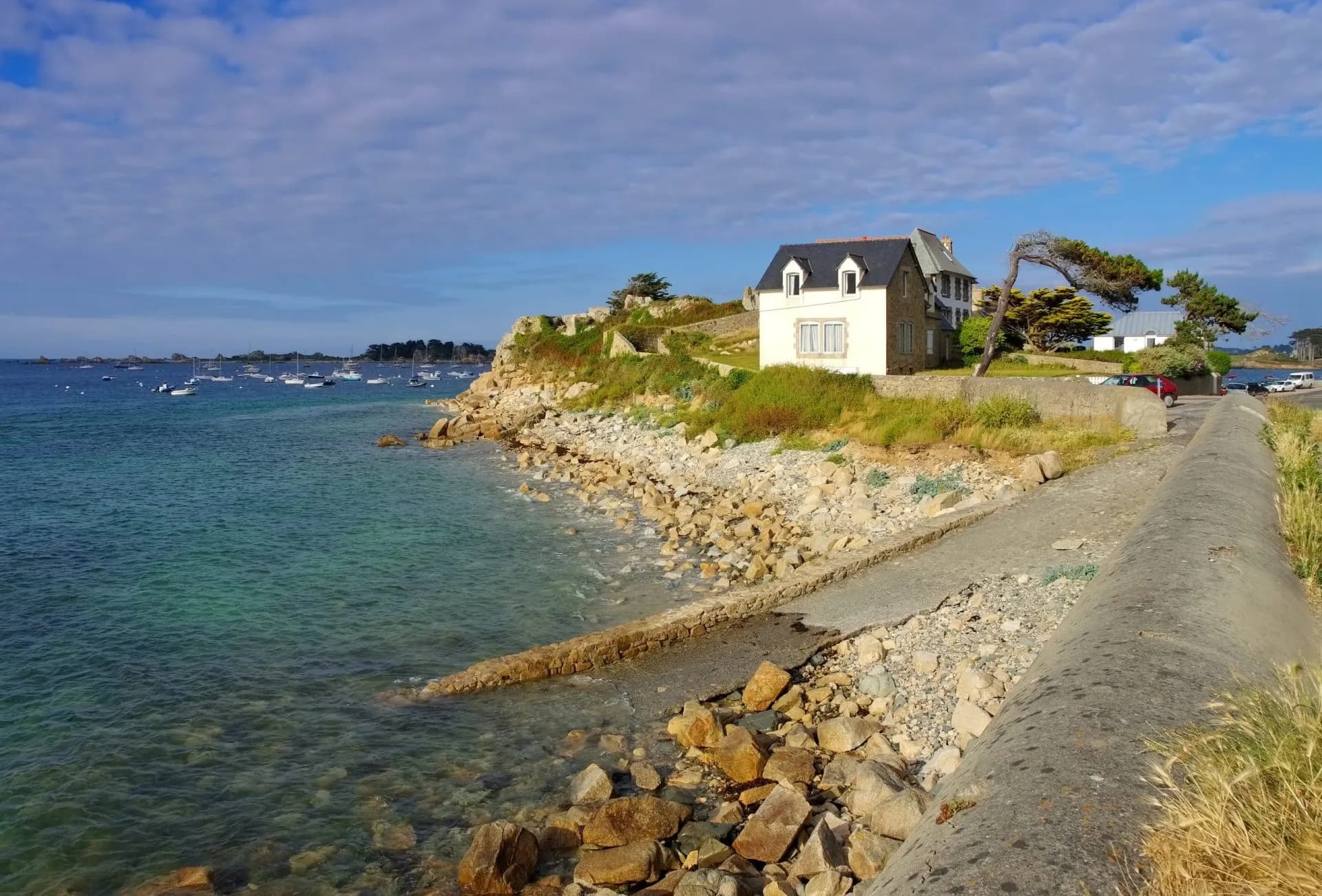 Footpath along rocky coast toward Port-Blanc with moored boats in clear blue water.
