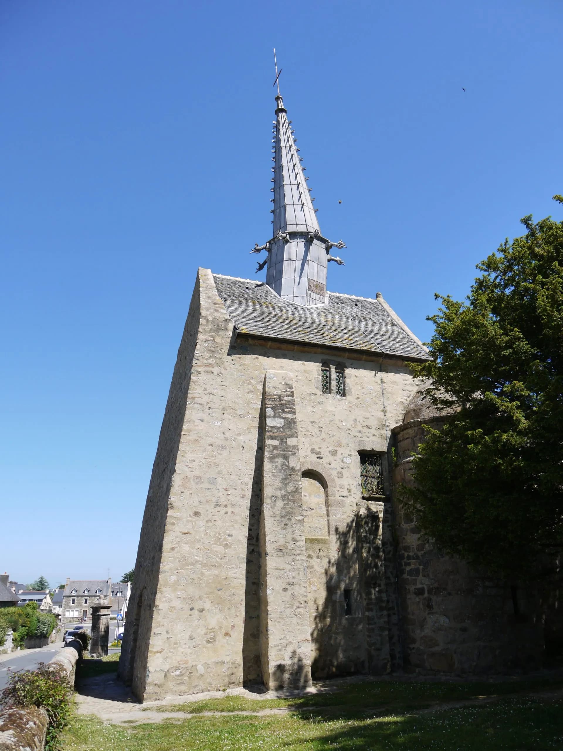 Stone church tower with slate spire and gargoyles under a clear blue sky at Castel Meur.