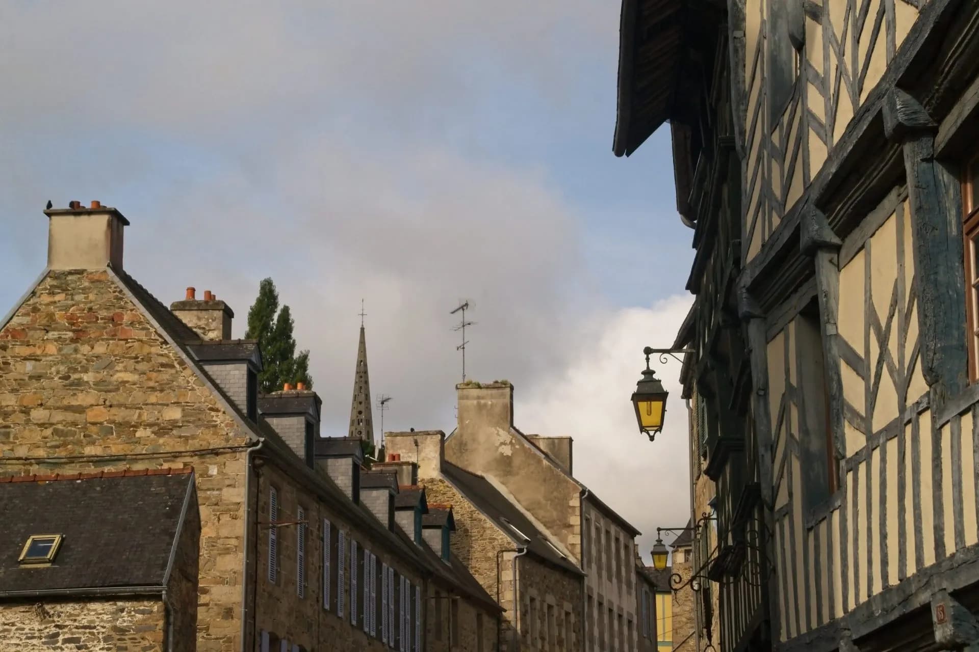 Rooftops and half-timbered buildings line a narrow street with a church spire in Rue de Treguier.