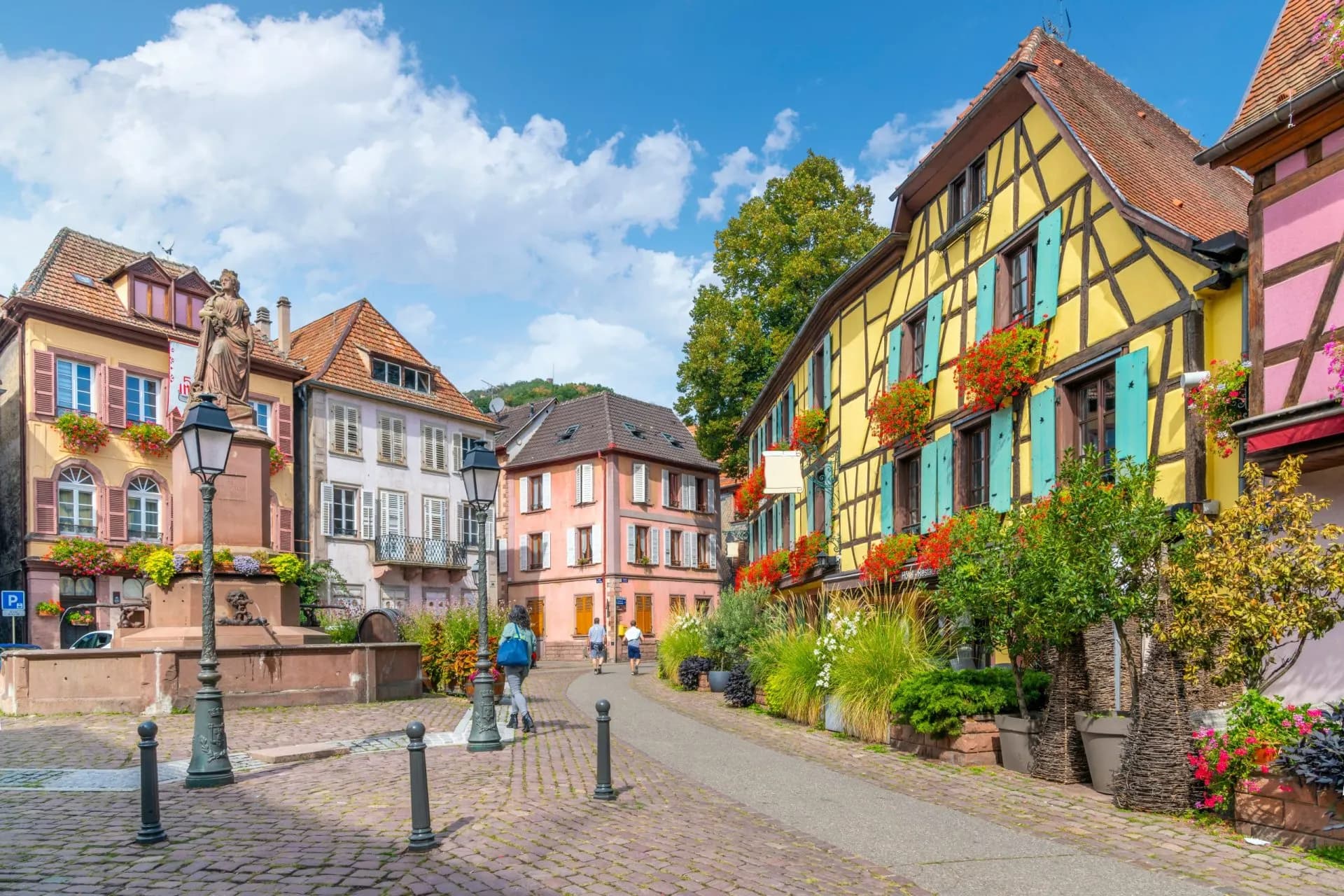 Ribeauvillé half-timbered buildings with flowers lining a cobblestone square and fountain.