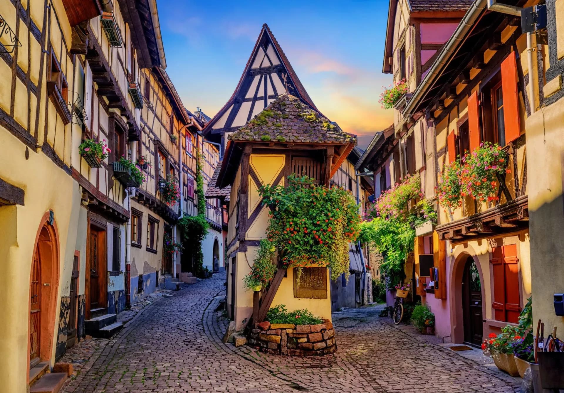 Colorful half-timbered houses line a steep cobblestone street in Eguisheim at sunset.
