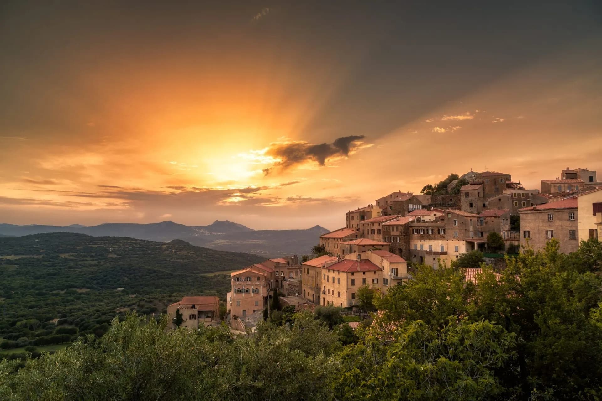 Hillside village with terracotta roofs at sunset over mountains in Corsica