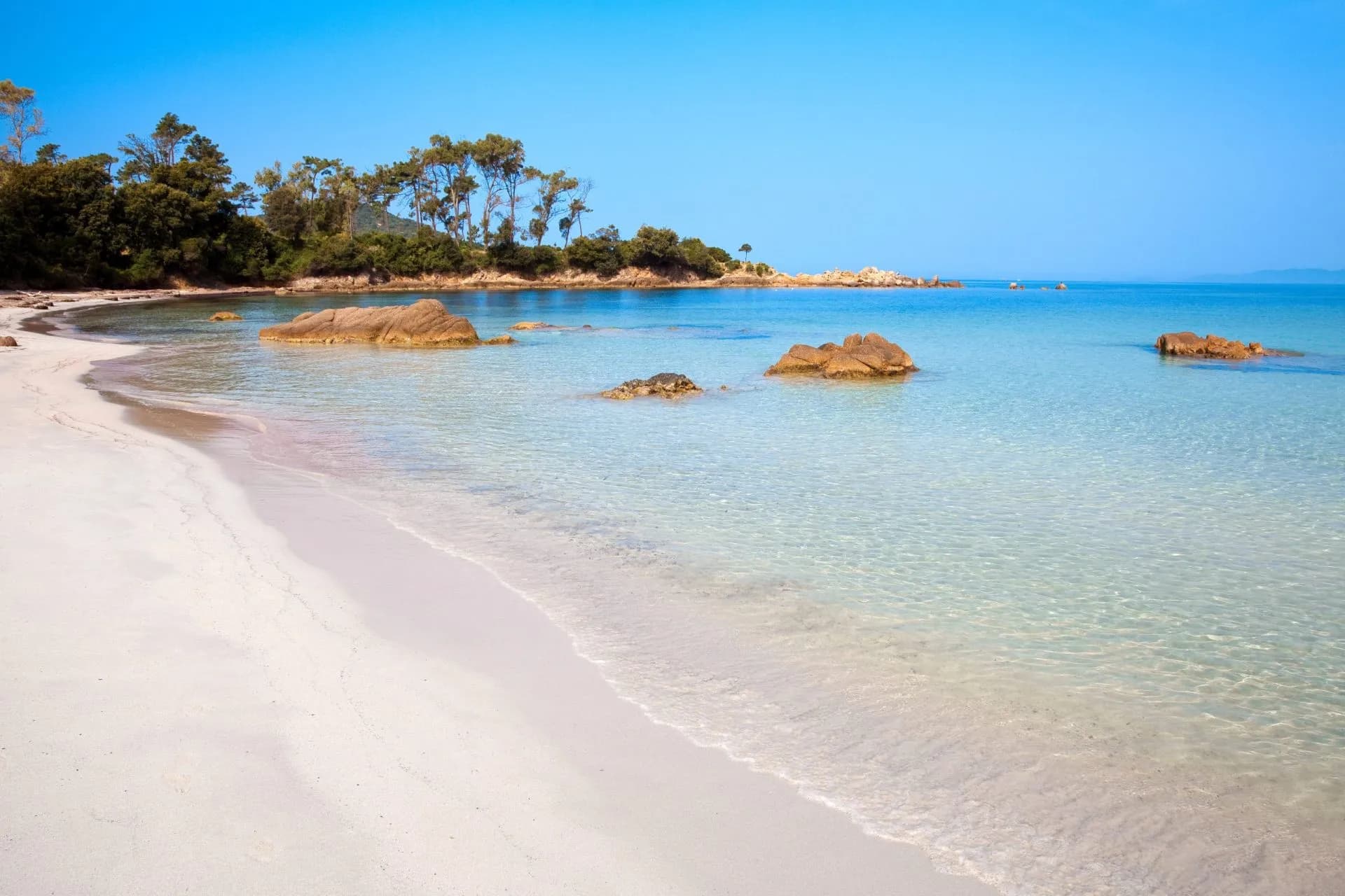 White sand beach with clear turquoise water and large rocks near Ajaccio coastline.
