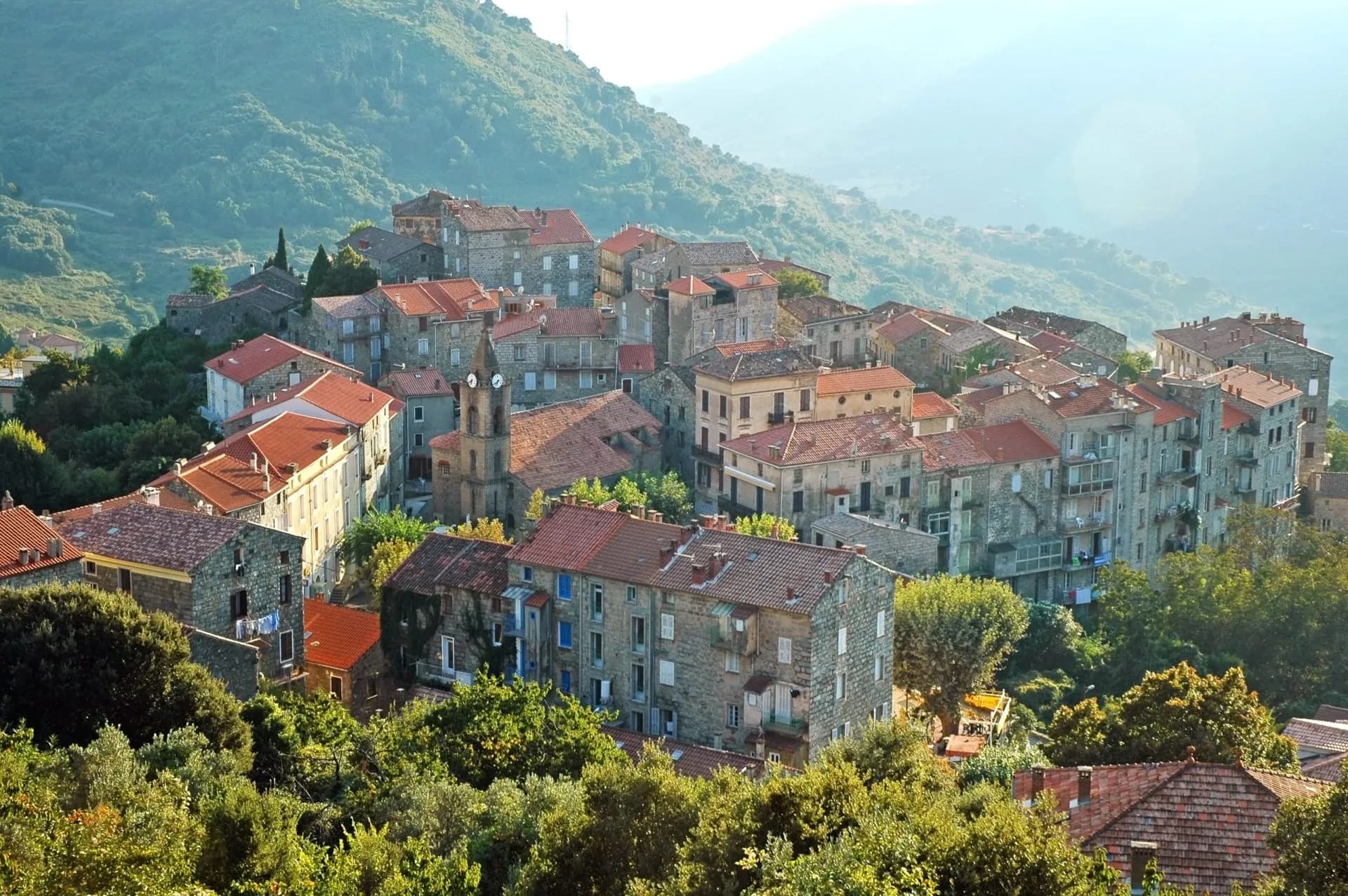 Stone village with red tile roofs nestled in lush green mountains, Corsica.