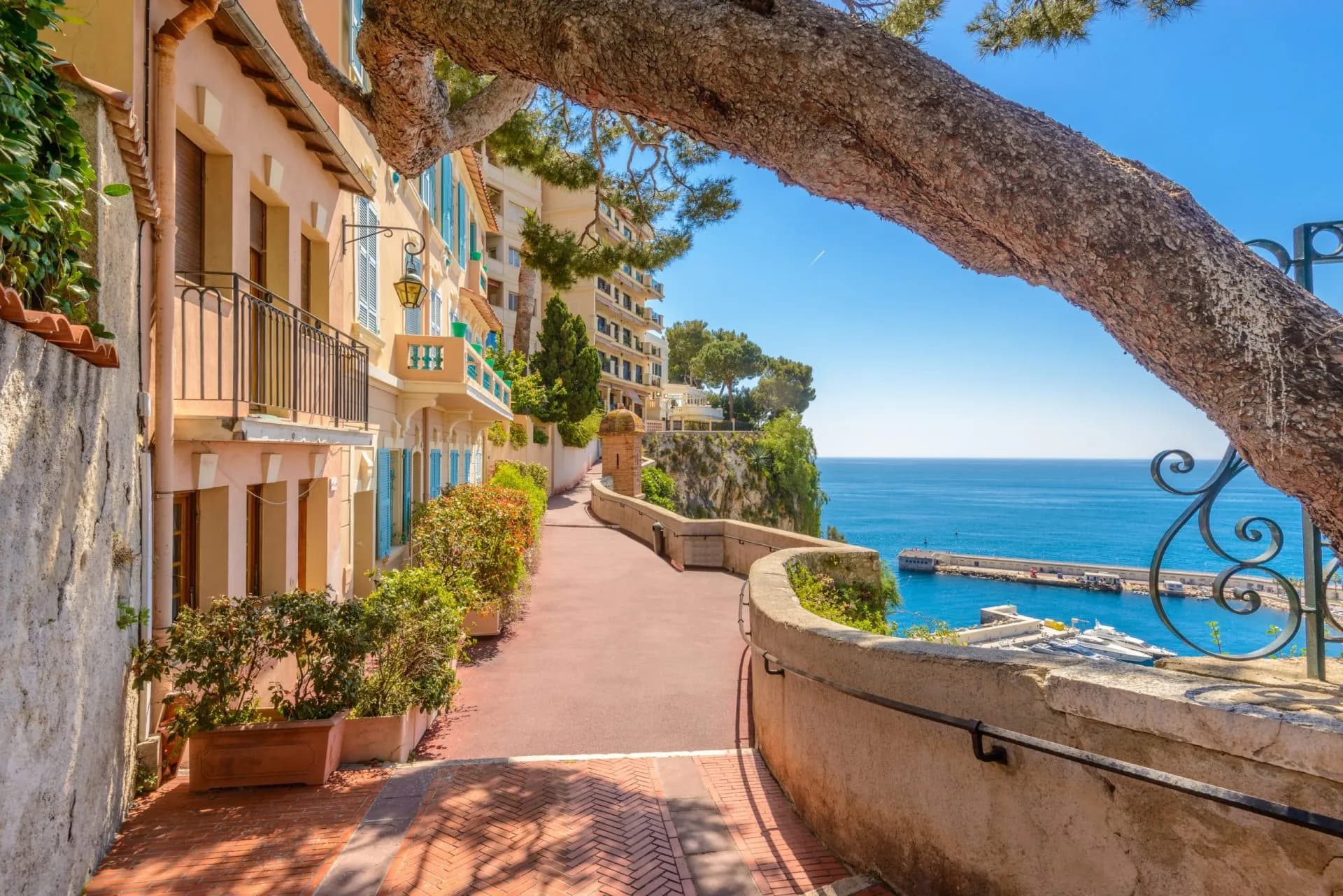 Winding pedestrian path past pastel buildings overlooking the blue Mediterranean Sea in Monaco.