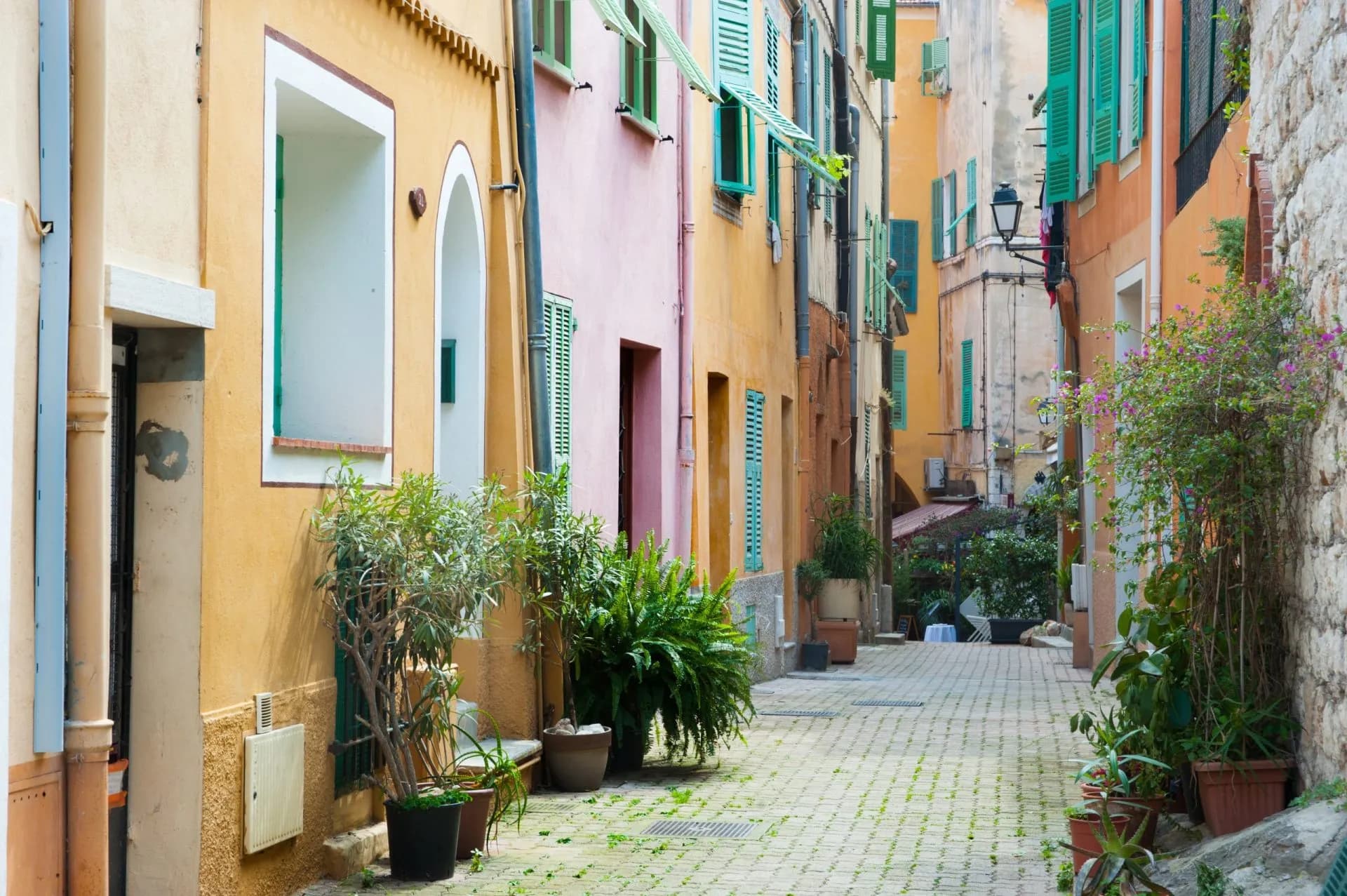 Narrow cobblestone street with colorful buildings and potted plants in Villefranche-sur-Mer.