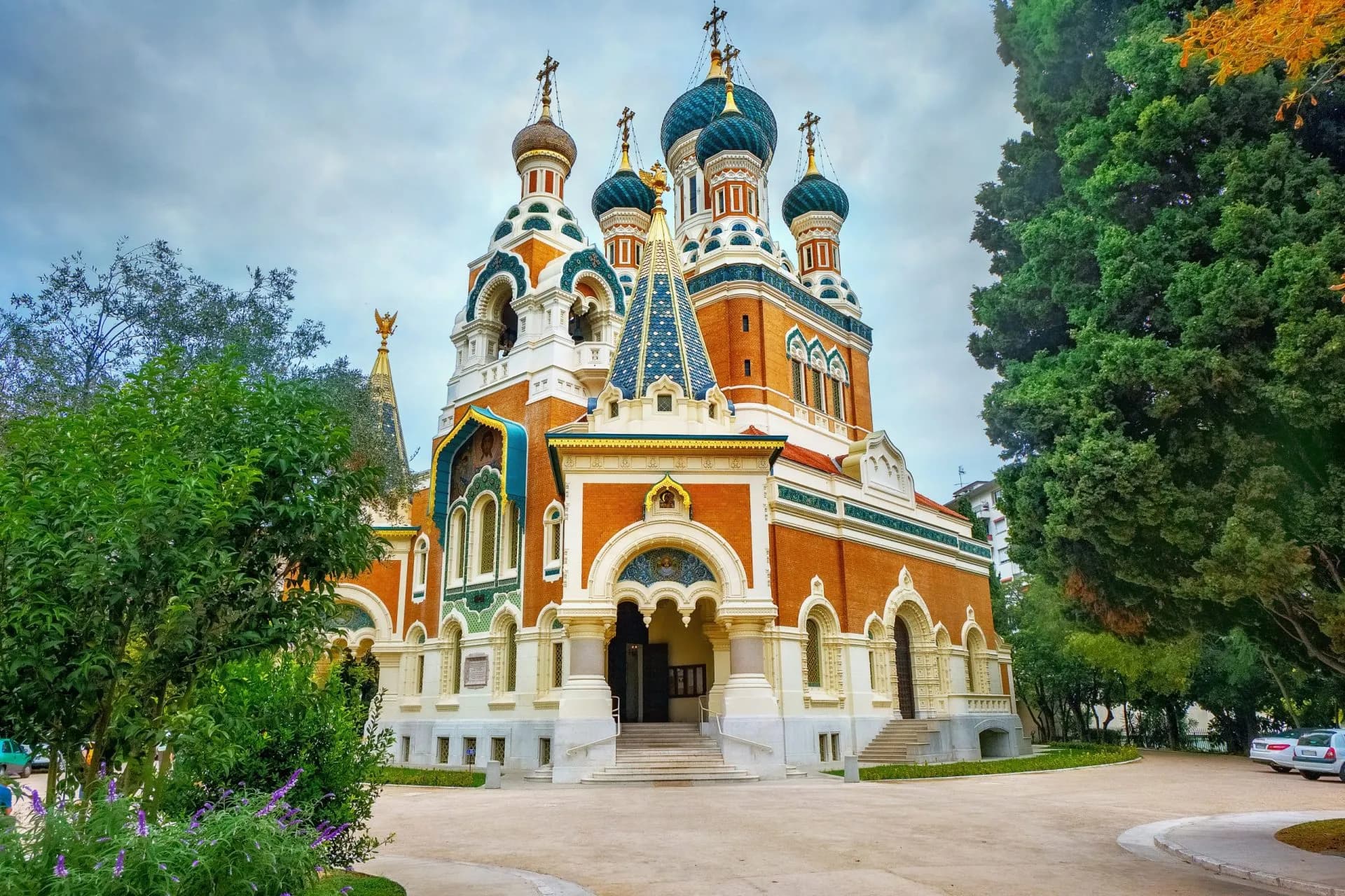 Russian Orthodox Cathedral of St. Nicolas in Nice with green trees and cloudy sky.