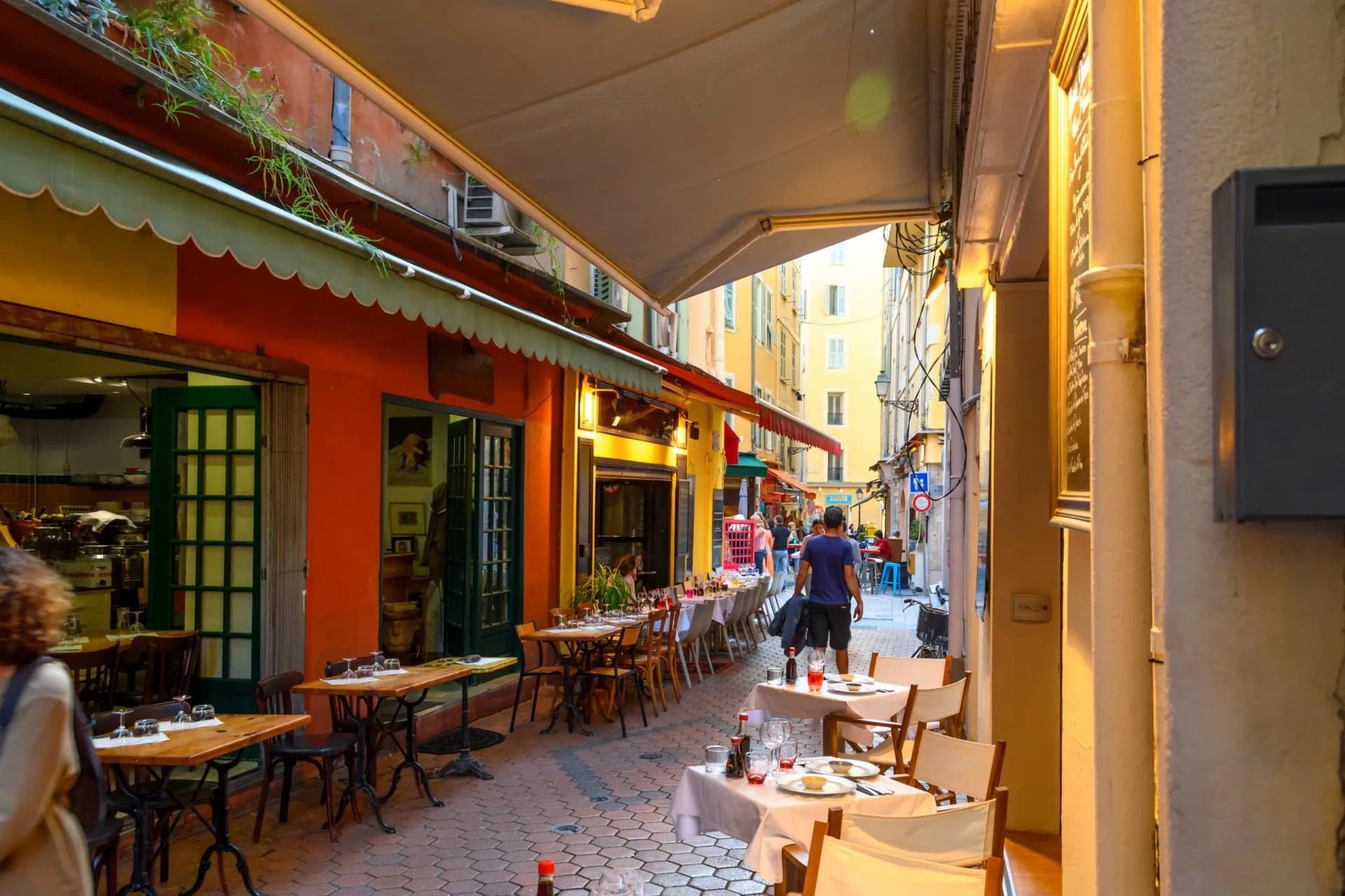 Outdoor dining tables on cobblestone alleyway in Vieux Nice with colorful buildings.