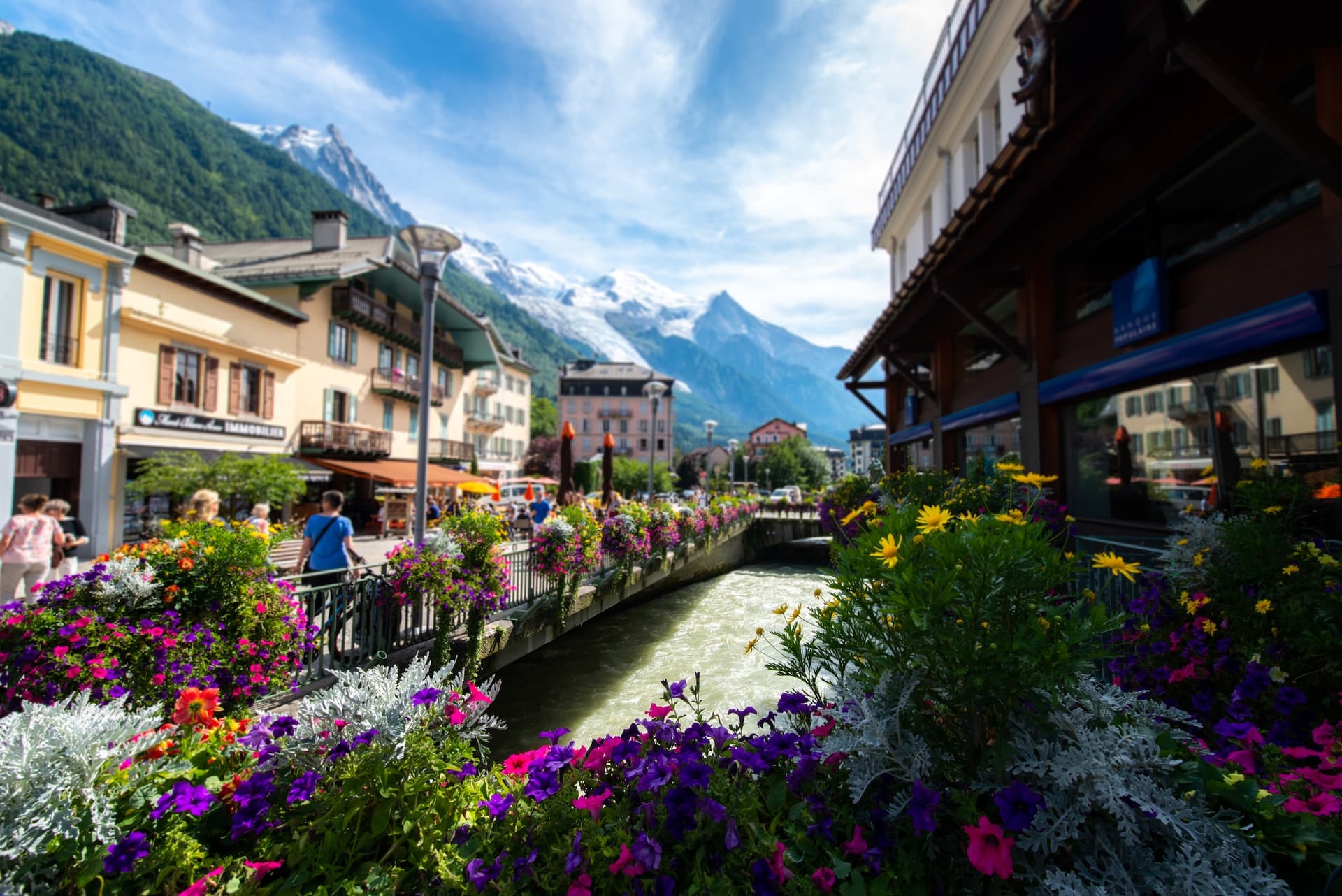 Chamonix town center with colorful flowers, rushing river, and snow-capped alpine mountains.