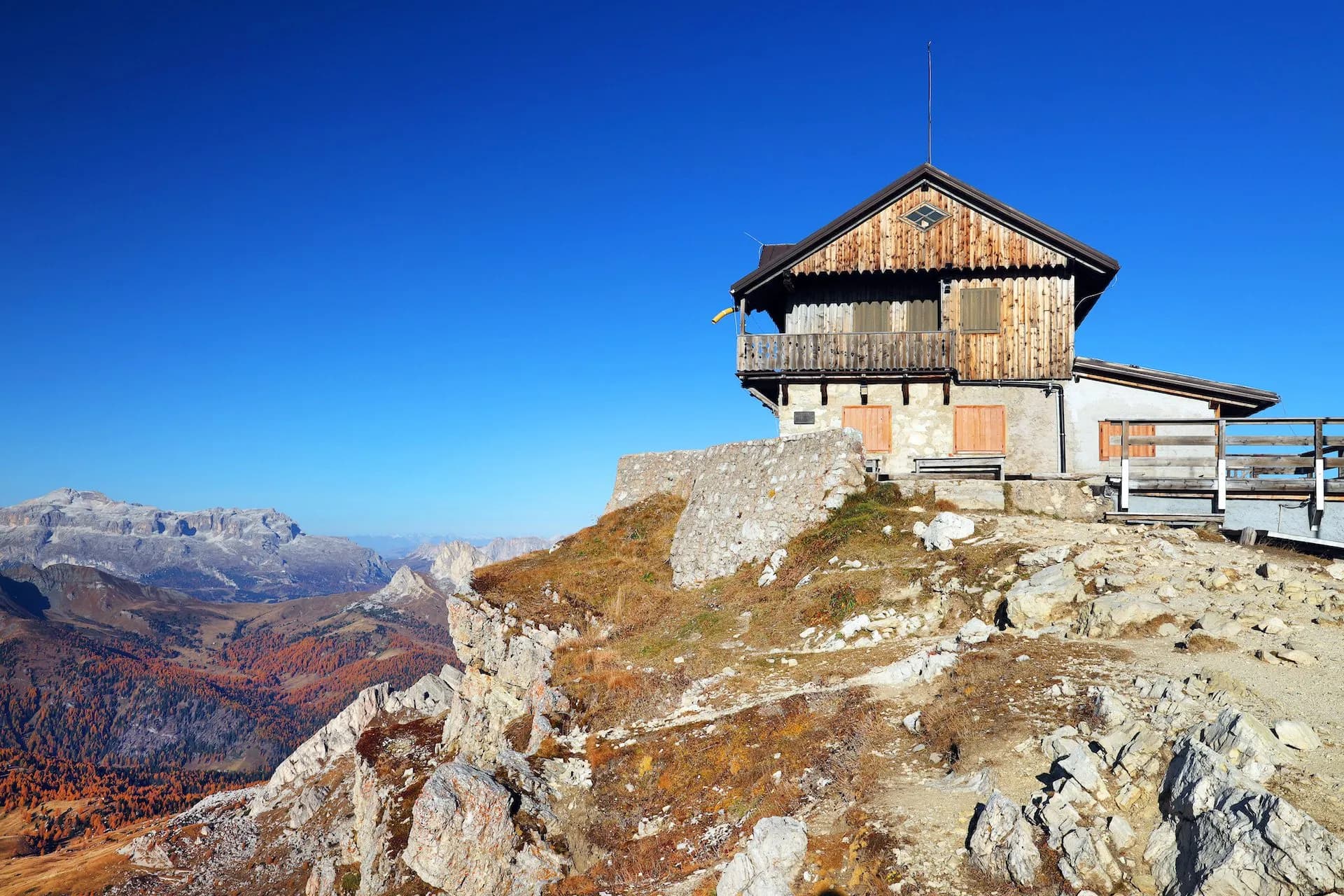 Rustic Rifugio Nuvolau mountain hut on rocky peak overlooking autumn-colored valleys and peaks.