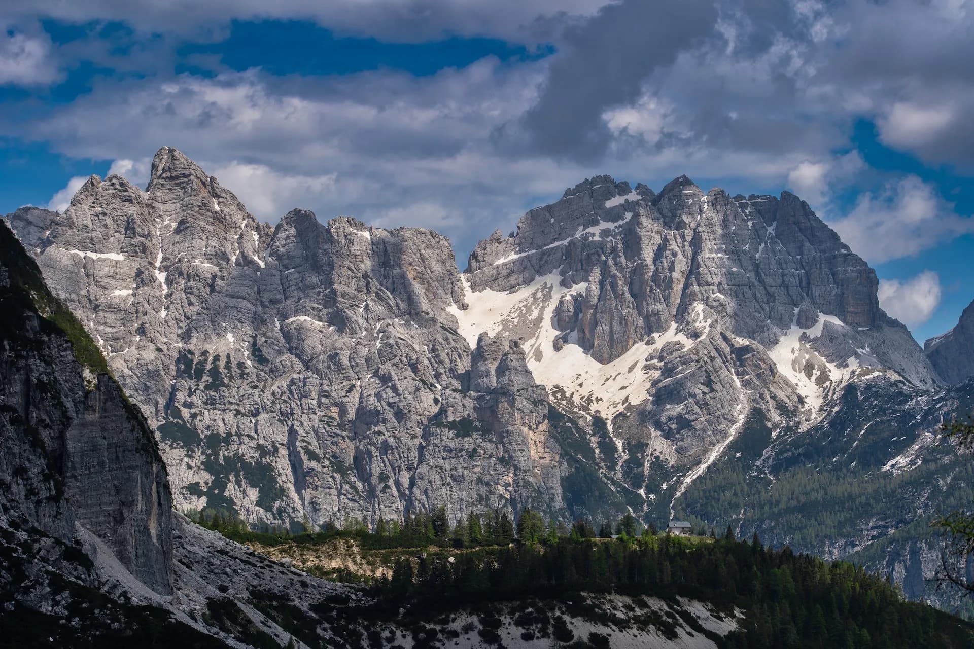 Rugged, rocky Rifugio Carestiato mountains with snow patches under a cloudy blue sky.