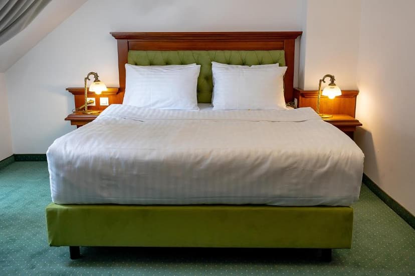 Hotel room with made bed, white linens, green base, and illuminated bedside lamps.