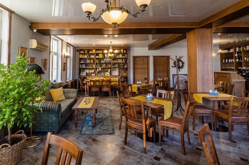 Interior of a cafe or restaurant with wooden tables, chairs, and a large bookshelf.