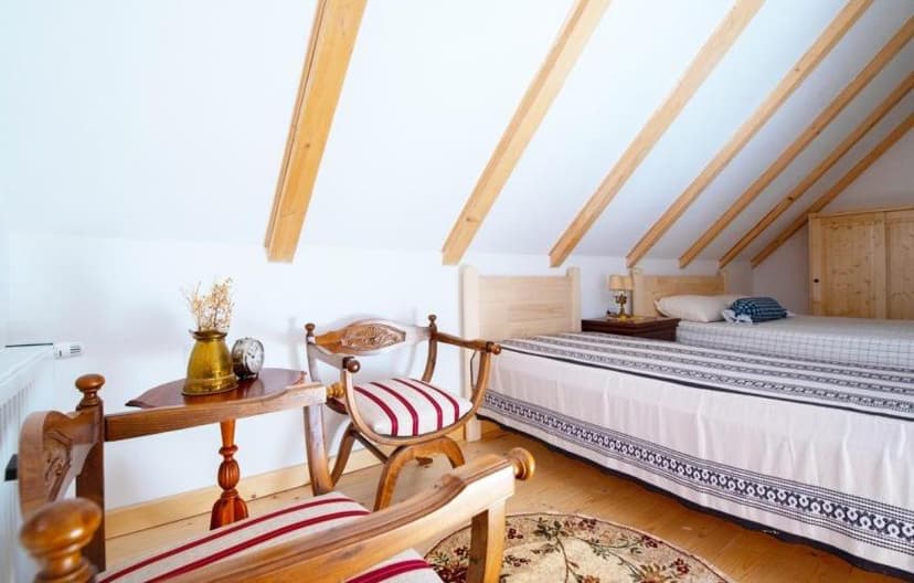 Attic bedroom with slanted wooden beams, light wood floor, and antique wooden chairs.