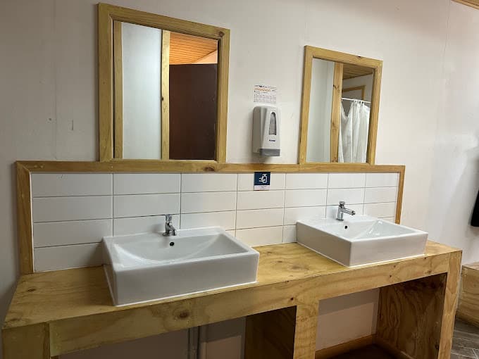 Two white square sinks set into a simple wooden vanity with mirrors above.