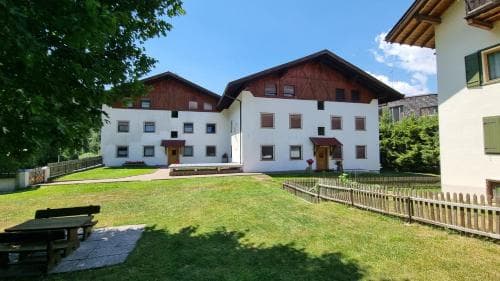 White alpine apartment building with wooden trim and grassy yard in Seis am Schlern.