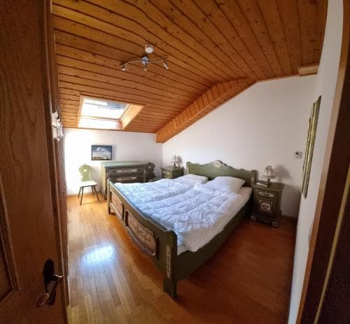 Attic bedroom with wood plank ceiling, green wooden bed, and skylight in Seis am Schlern.