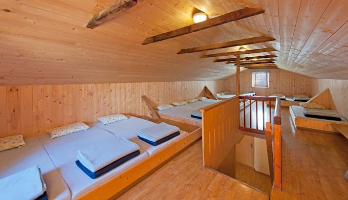 Dormitory sleeping area with wooden walls and floors in Rifugio Bolzano mountain hut.