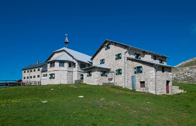 Stone mountain refuge Rifugio Bolzano under a clear blue sky with green meadow foreground