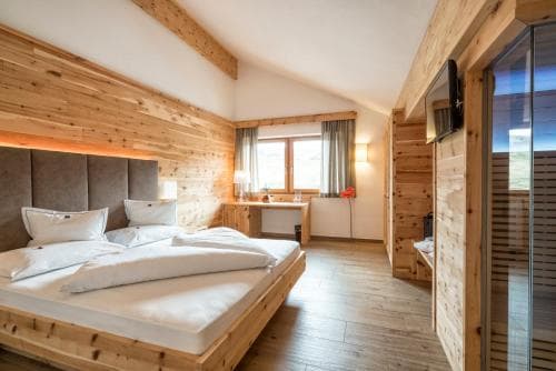 Alpine hotel room with wood paneling, large bed, and glass-fronted sauna area.