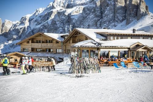 Ski resort restaurant in Passo Sella with skiers and snow-covered Dolomite mountains.