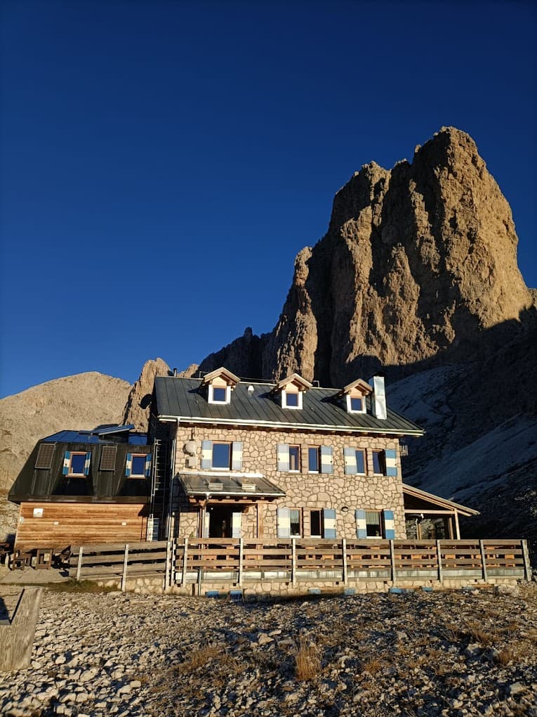 Rifugio Antermoia stone mountain hut below steep rock face under clear blue sky.