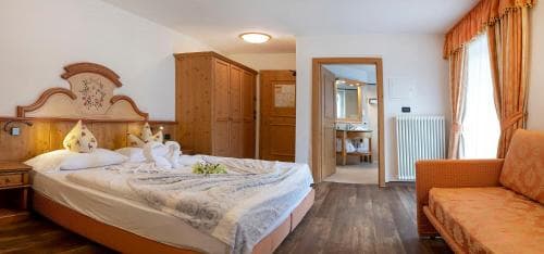 Hotel bedroom with wooden furniture, neatly made bed with towel swans, and orange sofa.
