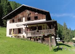 Alpine mountain refuge with wooden balcony on grassy slope surrounded by pine forest