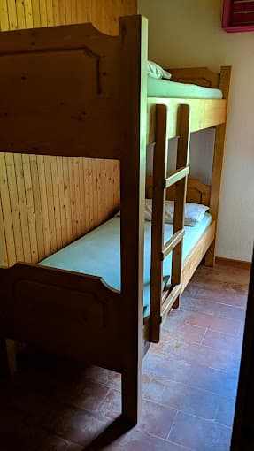Wooden bunk beds with light mattresses in a room with wood paneling and terracotta tile floor.