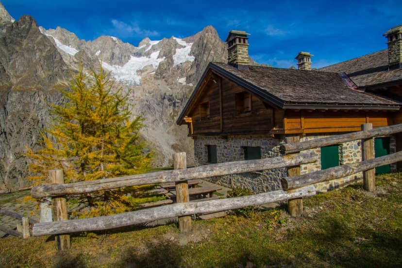 Alpine refuge with stone chimneys, wooden fence, and snowy peaks in background