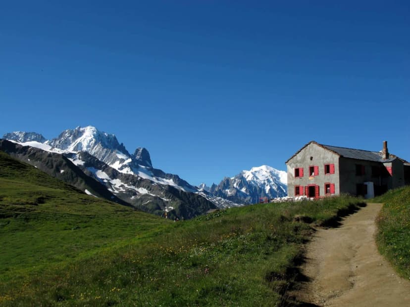 Refuge Col de Balme with snow-capped mountains and hiking path under clear blue sky.
