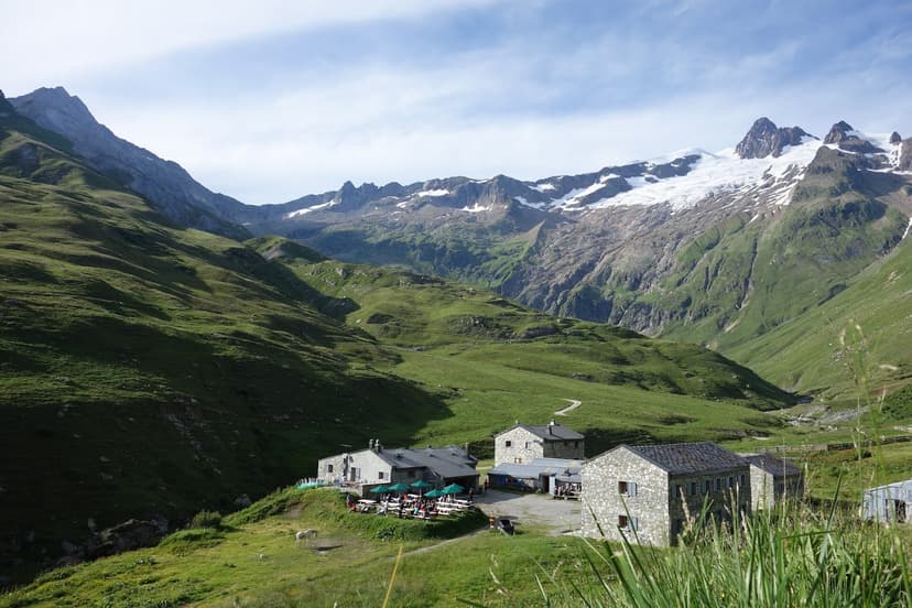 Refuge des Mottets stone buildings in green alpine valley with snow-capped mountains.