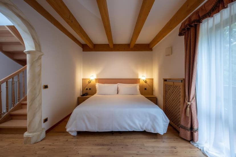 Hotel bedroom with white bedding, exposed wooden ceiling beams, and wooden staircase access.