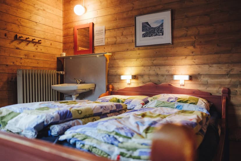 Cozy DNT cabin room with wood paneling, beds, sink, and mountain art at Gjendesheim.