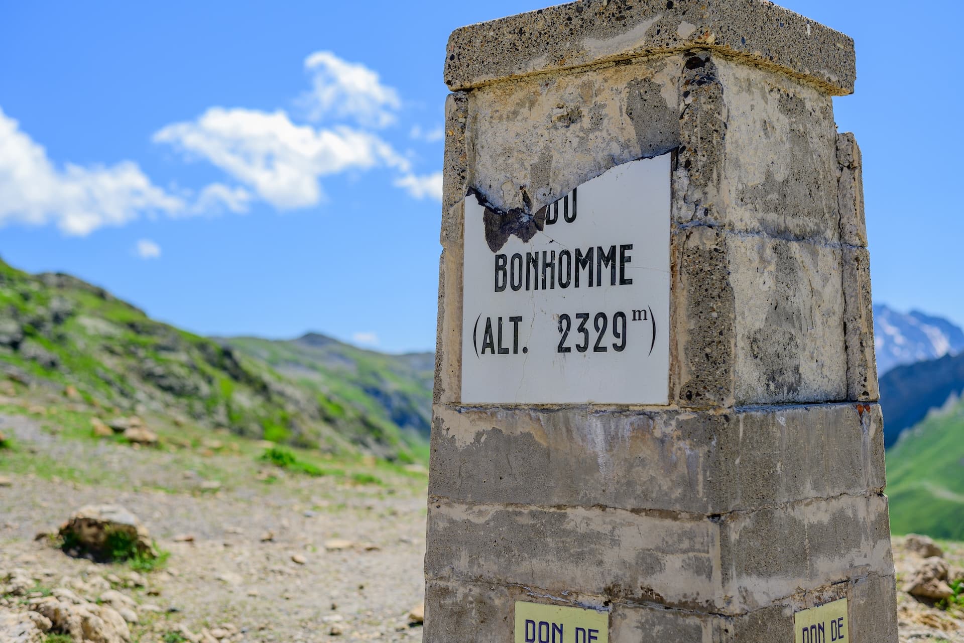 Col de Bonhomme altitude marker (2329m) on hiking trail with green mountains and blue sky.
