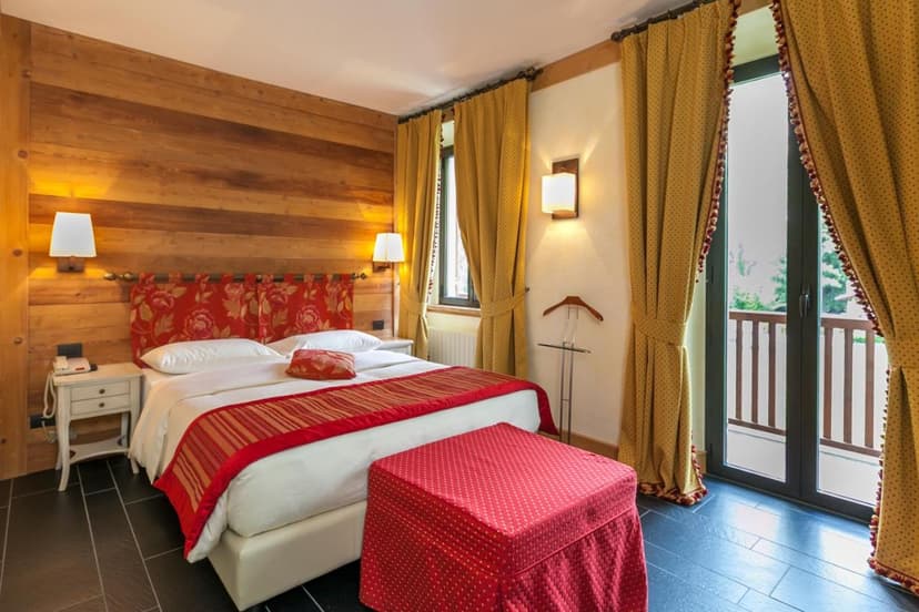 Hotel bedroom with wood paneling, red and white bedding, and balcony access at Hotel Lo Scoiattolo.