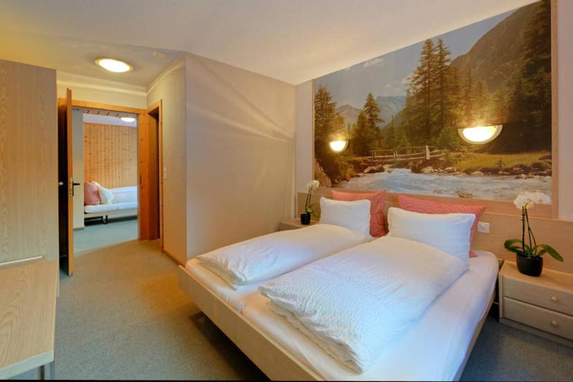 Hotel room with twin beds, mountain mural, and view into an adjoining room.